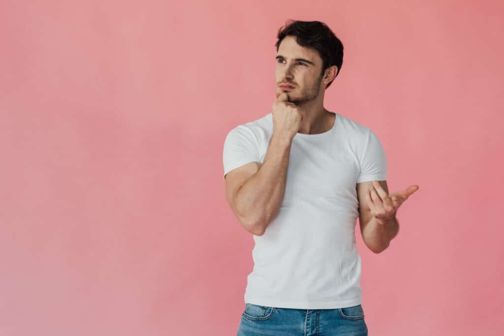 pensive muscular man in white t-shirt propping face with fist and counting on fingers isolated on pink pensive muscular man in white t-shirt propping face with fist and counting on fingers isolated on pink