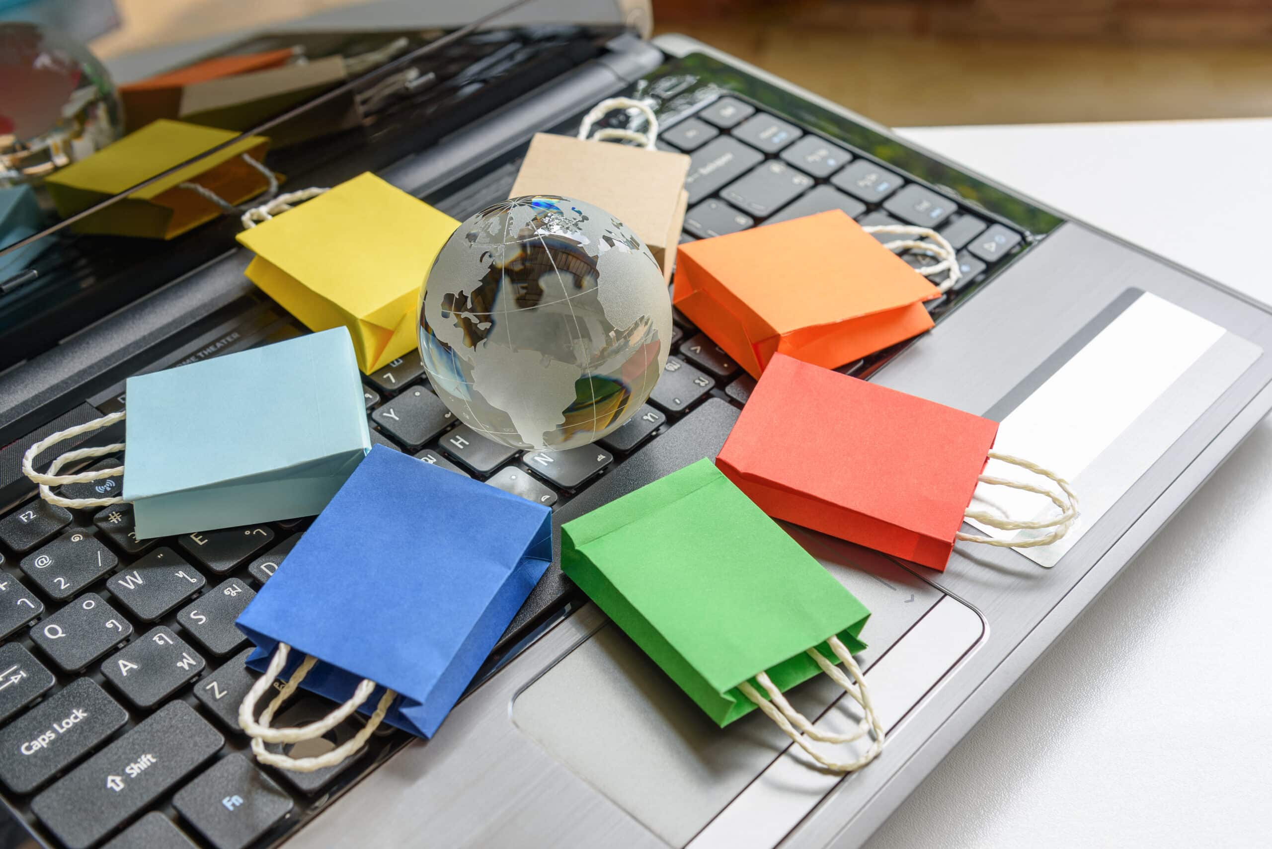 Various shopping bags surrounding a globe on a desk with a laptop