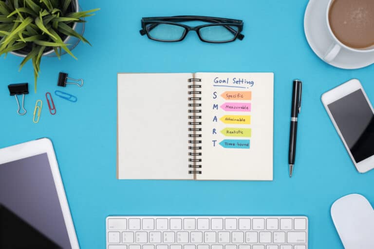 smart-goal-setting-with-office-supplies-blue-desk A notebook with Smart Goals written on it