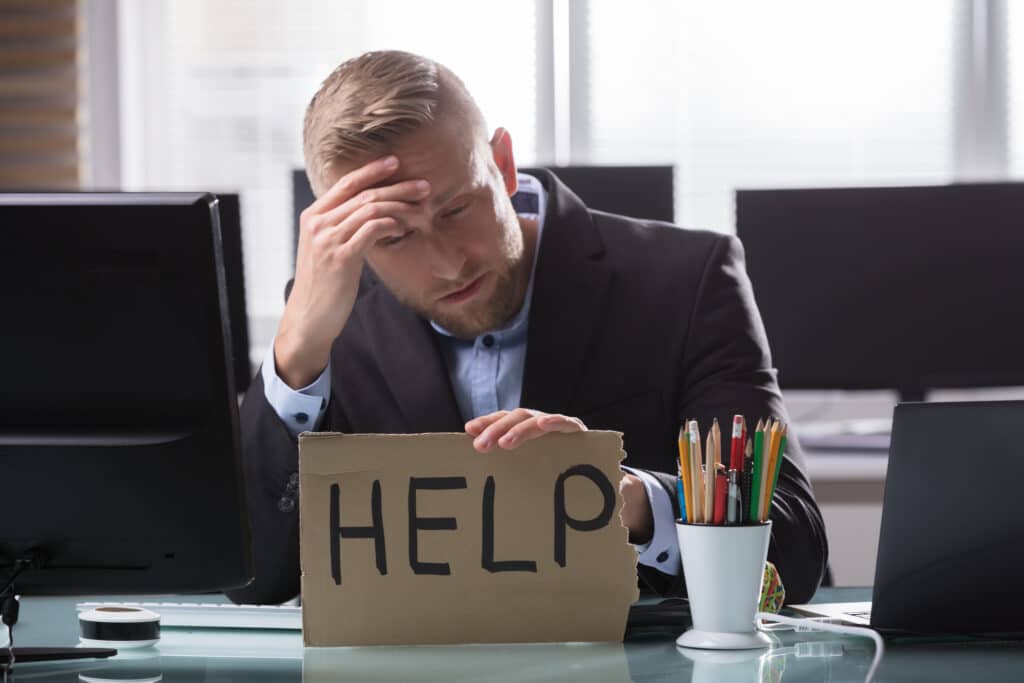 Businessman Holding Cardboard With Help Text A business man at his desk with a sign asking for help